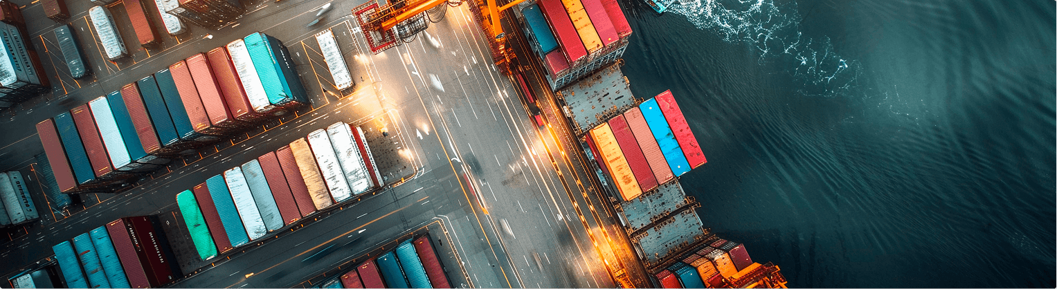 Vista aérea de um porto com contêineres coloridos organizados e guindastes próximos ao mar.
